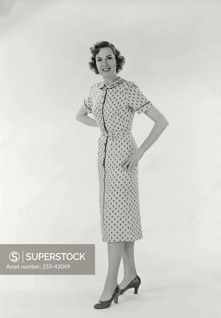 Vintage Photograph. Full length view of woman standing on white background wearing diamond patterned dress with hands on hips