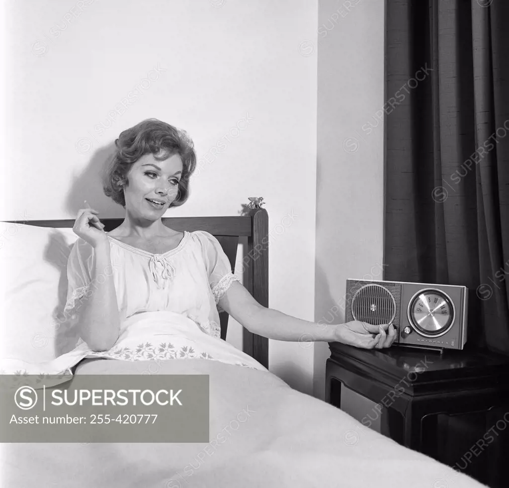 Portrait of mid adult woman reclining in bed and listening to the radio