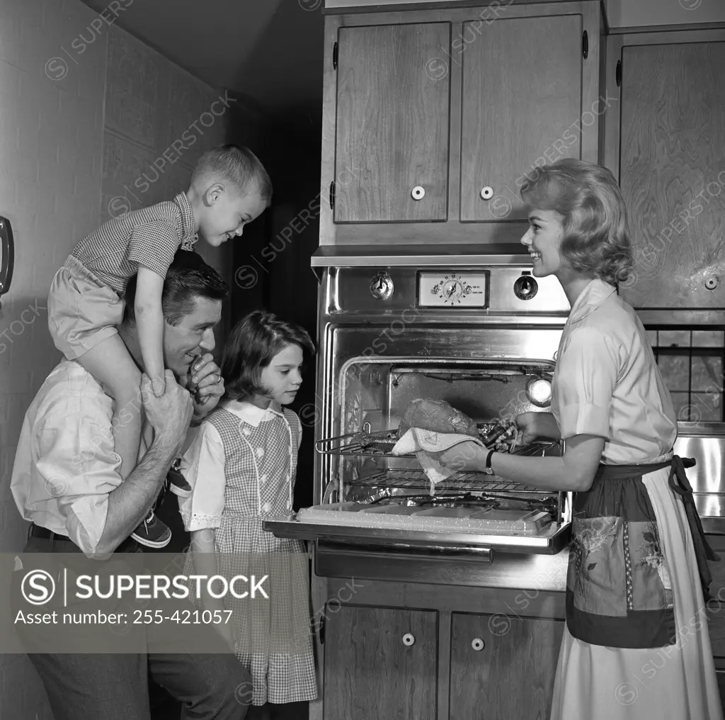 Mother showing freshly baked chicken to husband and children
