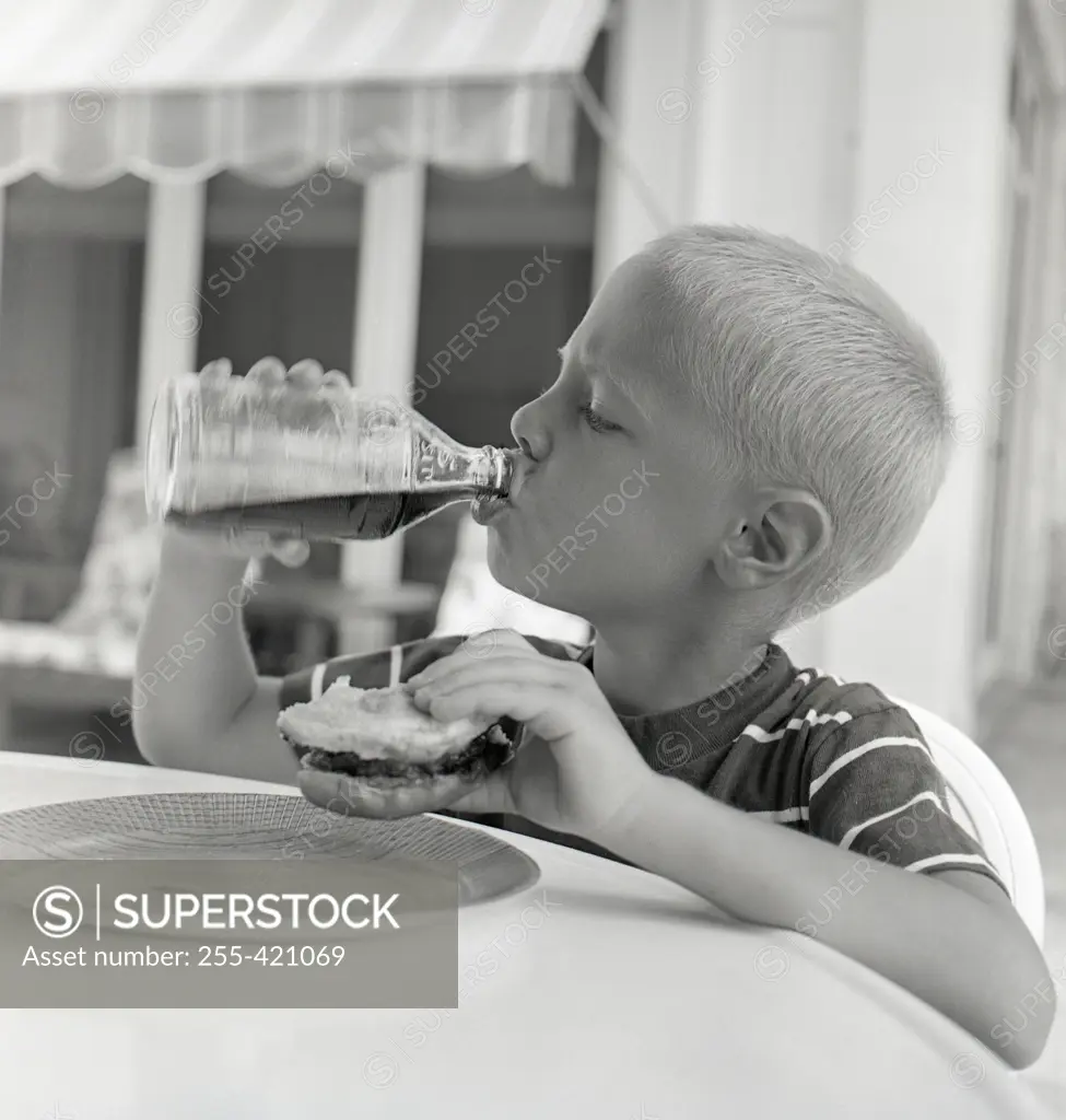 Boy drinking juice from bottle while holding sandwich