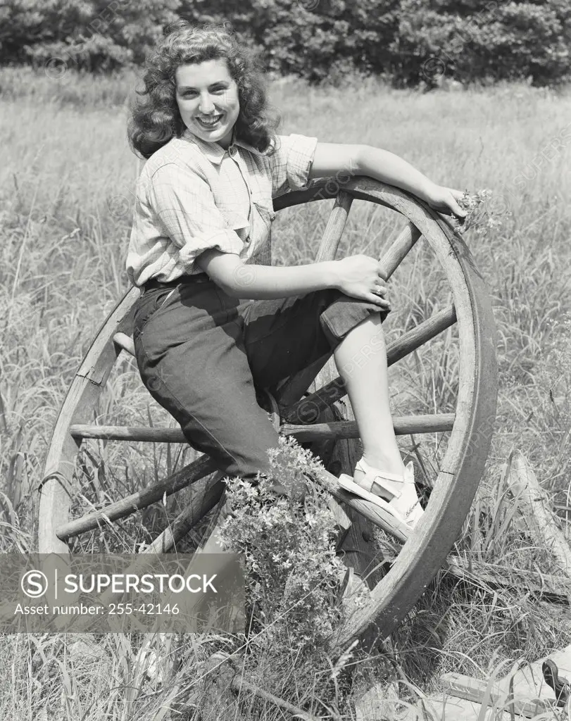 Young woman sitting on a wagon wheel and smiling