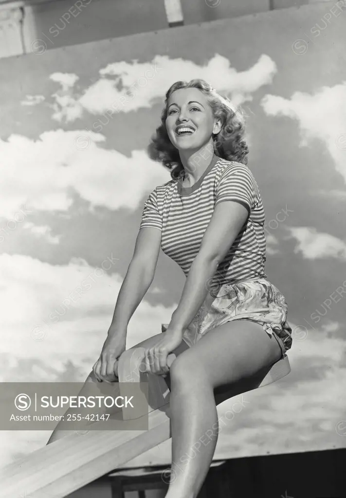 Vintage photograph. Low angle view of young woman in striped shirt sitting on seesaw