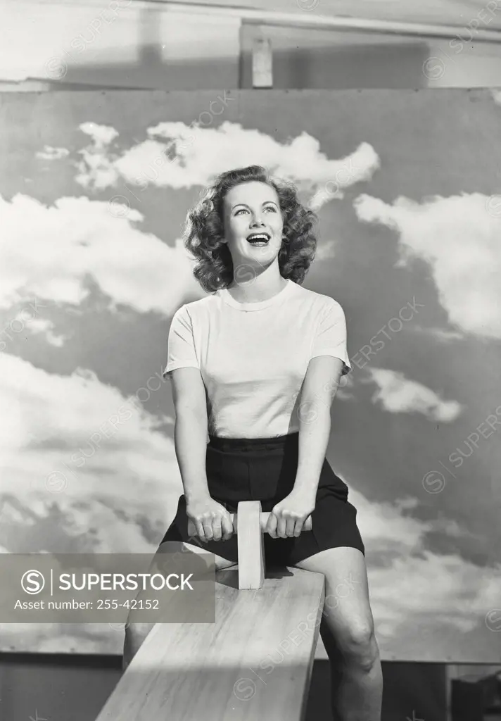 Vintage photograph. Low angle view of a young woman in t-shirt sitting on a seesaw