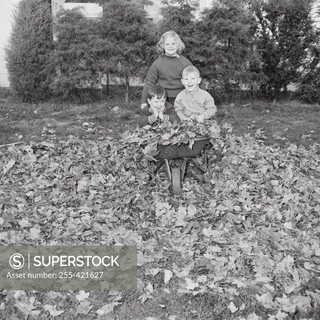 Sister carrying her younger brothers in wheelbarrow and looking at camera