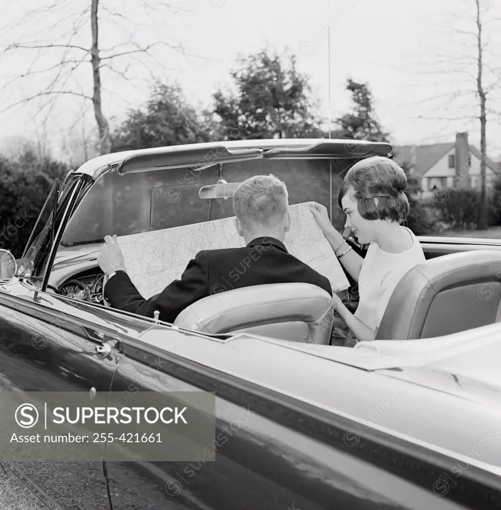 Young couple in convertible car reading map