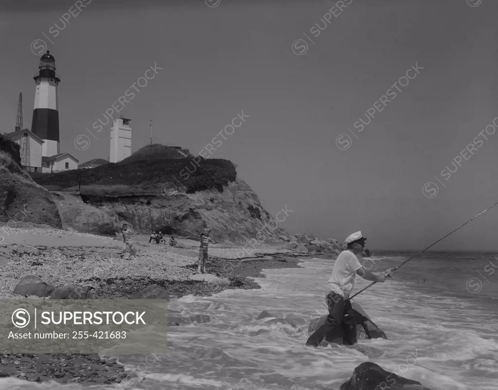 People fishing on seaside, lighthouse in the background
