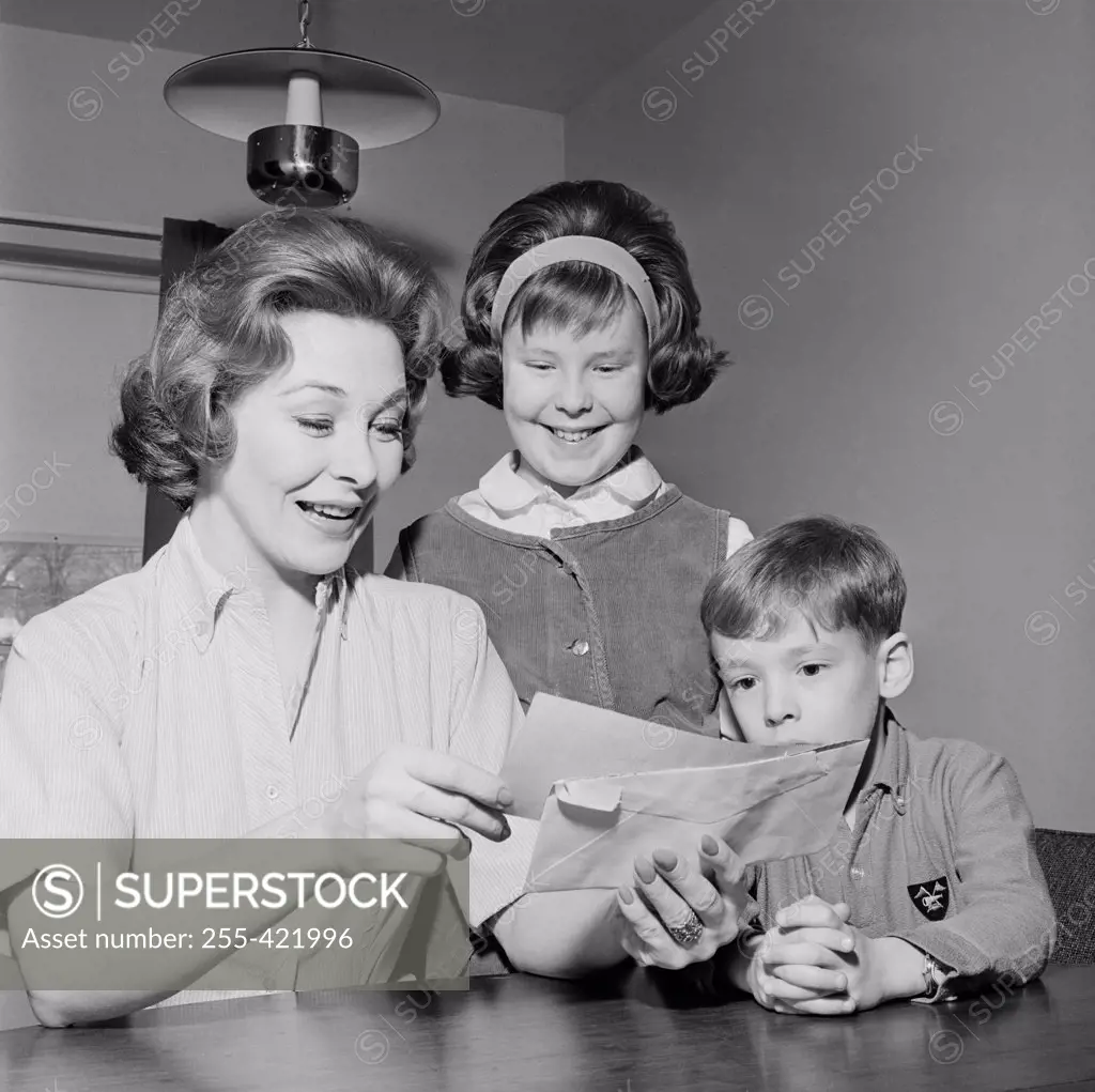 Girl and boy are watching as cheerful mother is reading letter