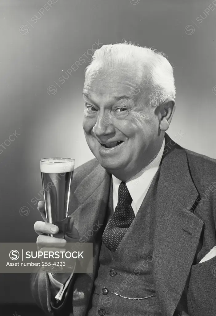 Vintage photograph. Elderly white haired gentleman holding up glass of beer smiling