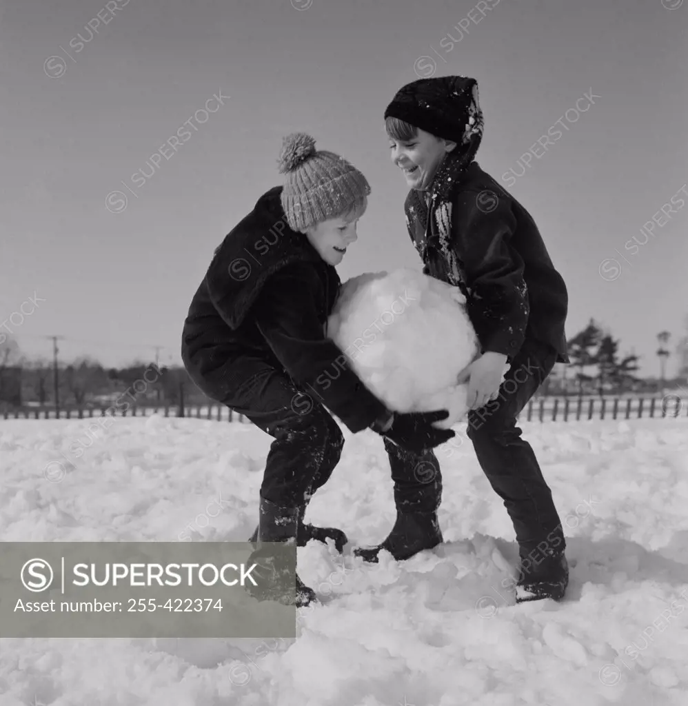 Two kids carrying large snowball