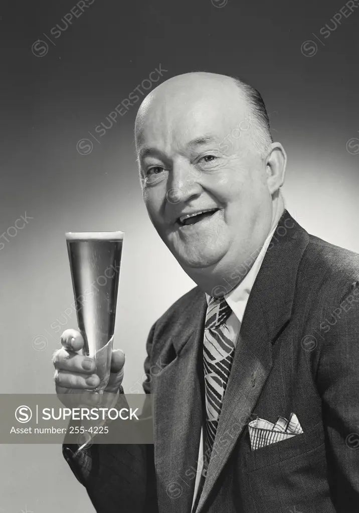 Older bald man in suit and tie smiling holding glass.