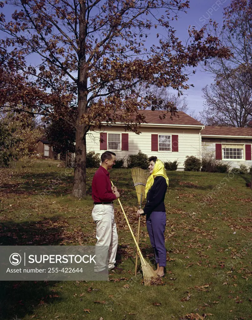 Young couple raking leaves in backyard