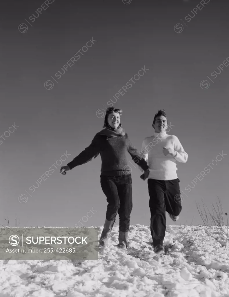 Young couple running down snowy hill