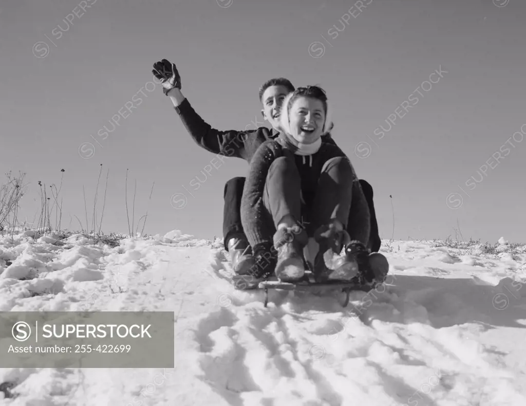Young couple sledding down snowy hill
