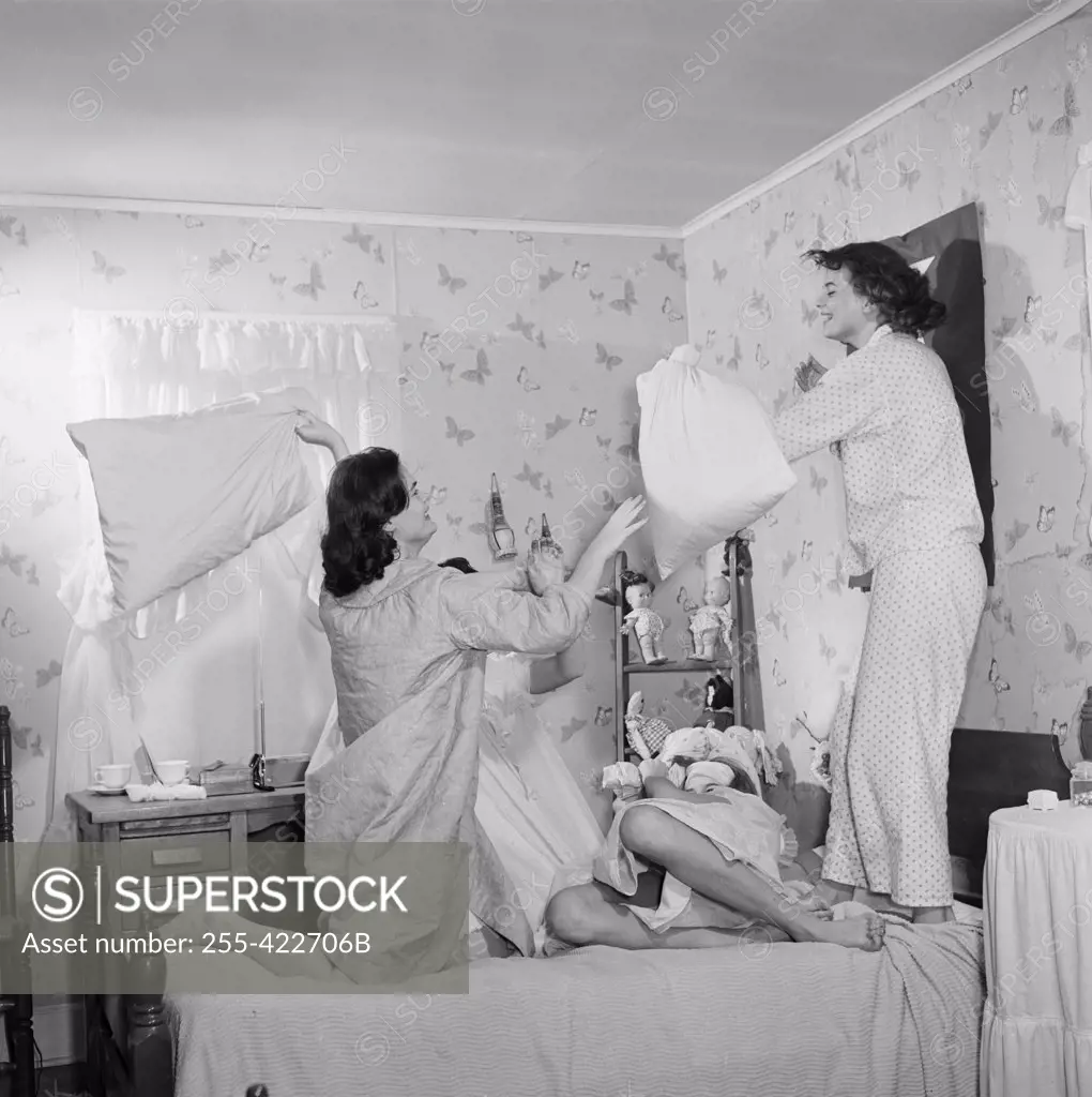 Four young women having pillow fight in bedroom