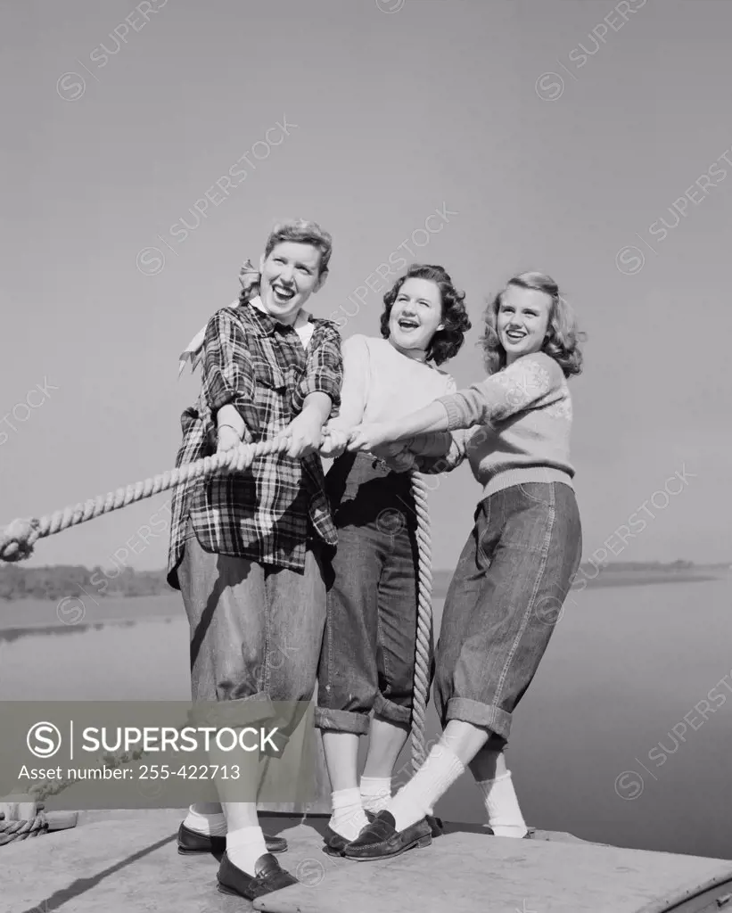 Three girls pulling rope on jetty