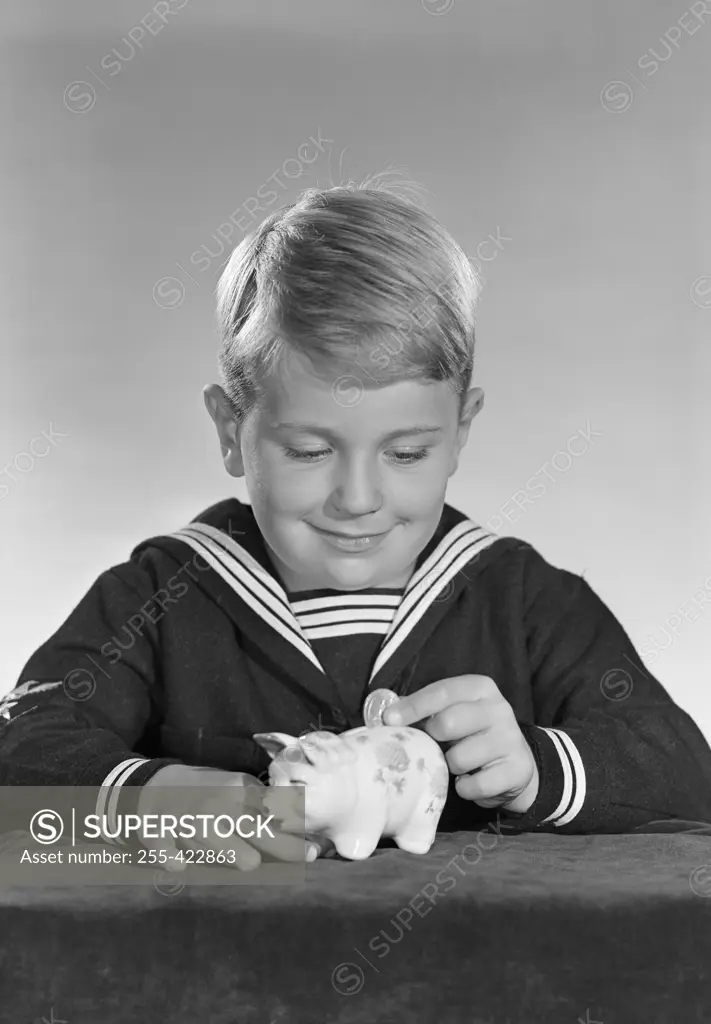Studio shot of boy inserting coin into piggy bank