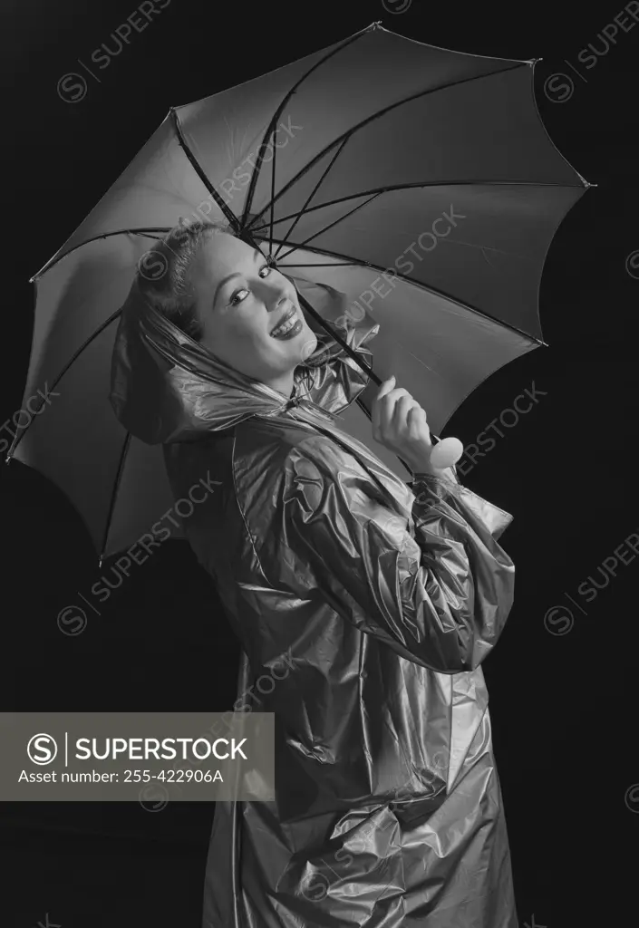Young woman holding umbrella and wearing raincoat