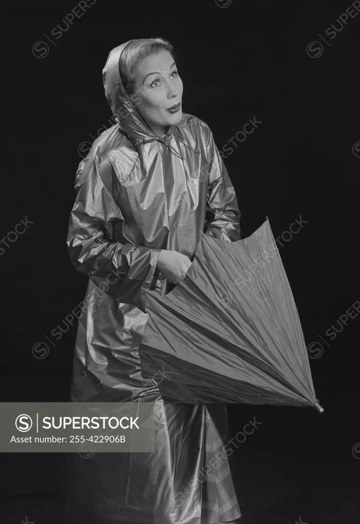 Young woman wearing raincoat opening umbrella