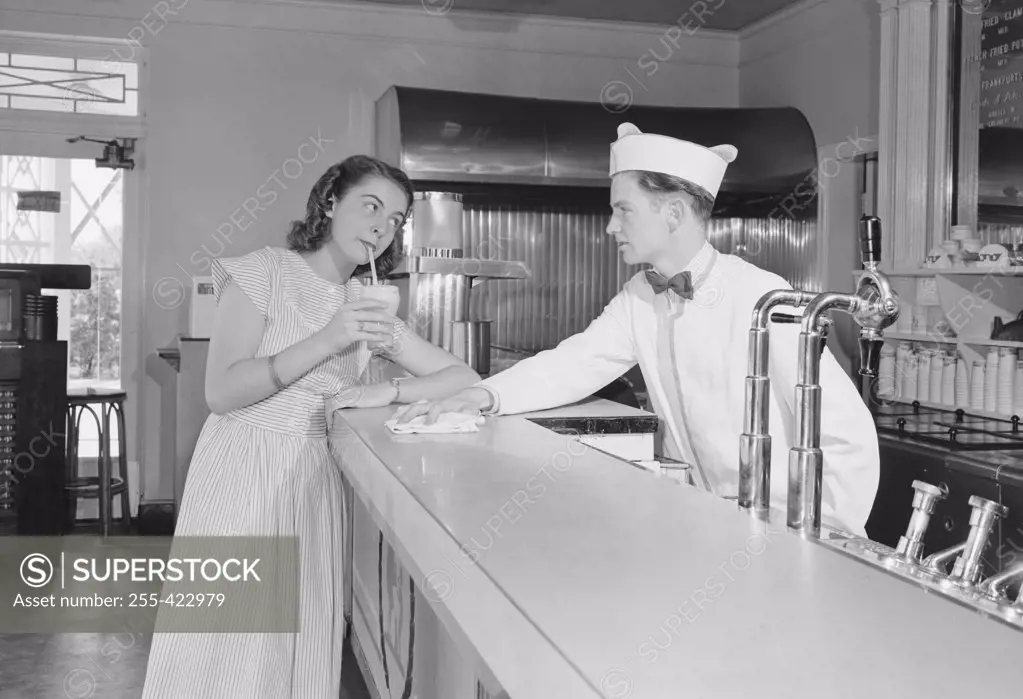 Young woman drinking milkshake at bar counter with barman