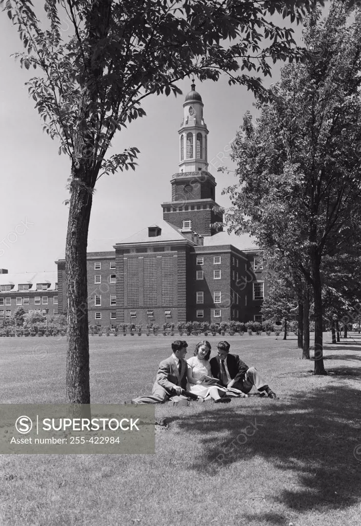 Three students sitting on grass outside university building
