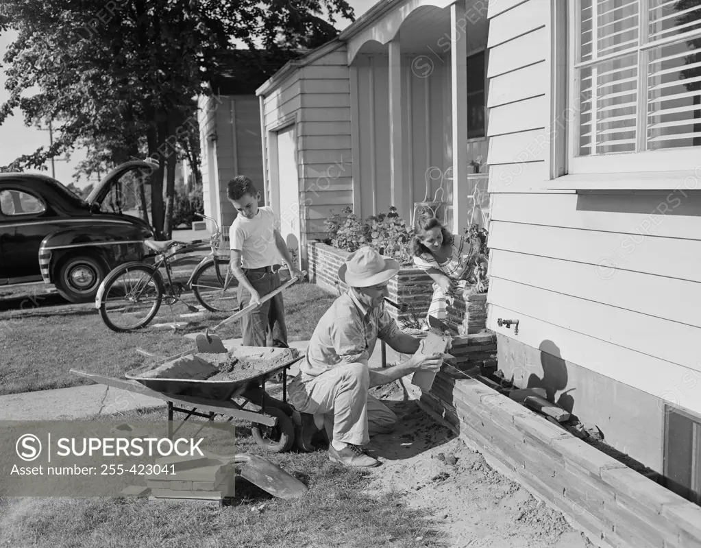 Boy and farther doing small masonry work outside suburban home
