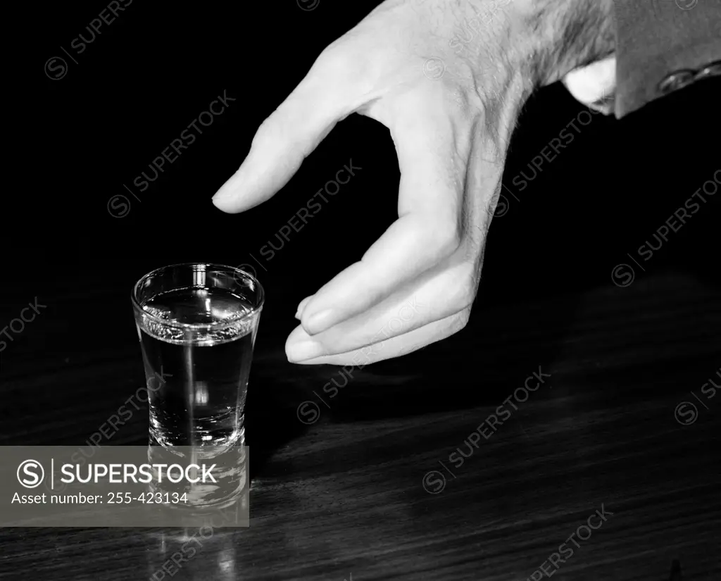 Close-up of hand nearly holding shot glass with alcohol