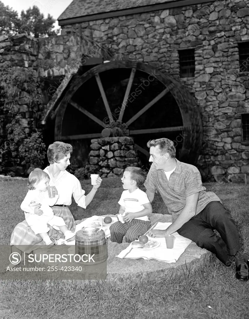 Family with baby girl and boy on picnic by water mill