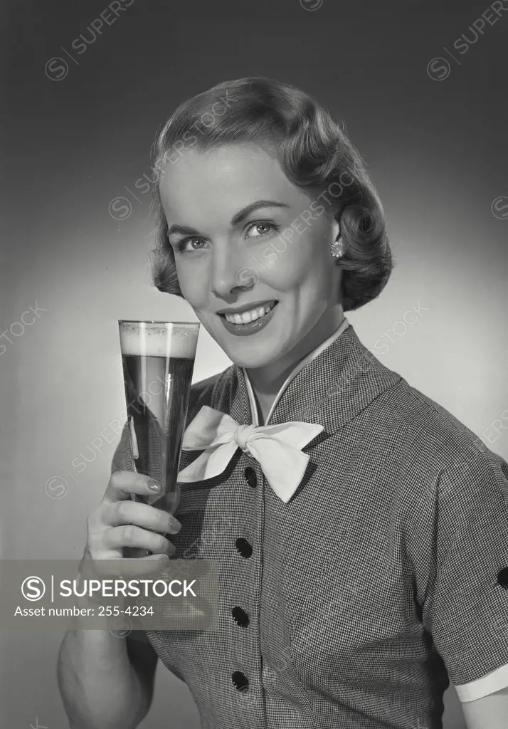 Vintage photograph. Woman in button blouse with bow smiling at camera and holding up glass