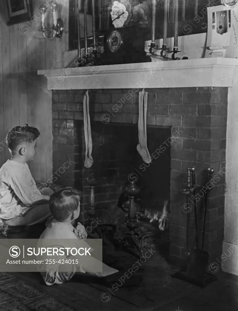 Two boys (4-5) sitting in front of fireplace looking at christmas stockings