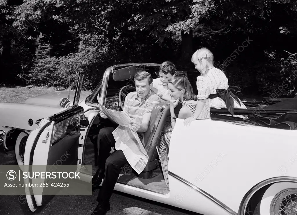 Family with boy and girl sitting in convertible car, examining map