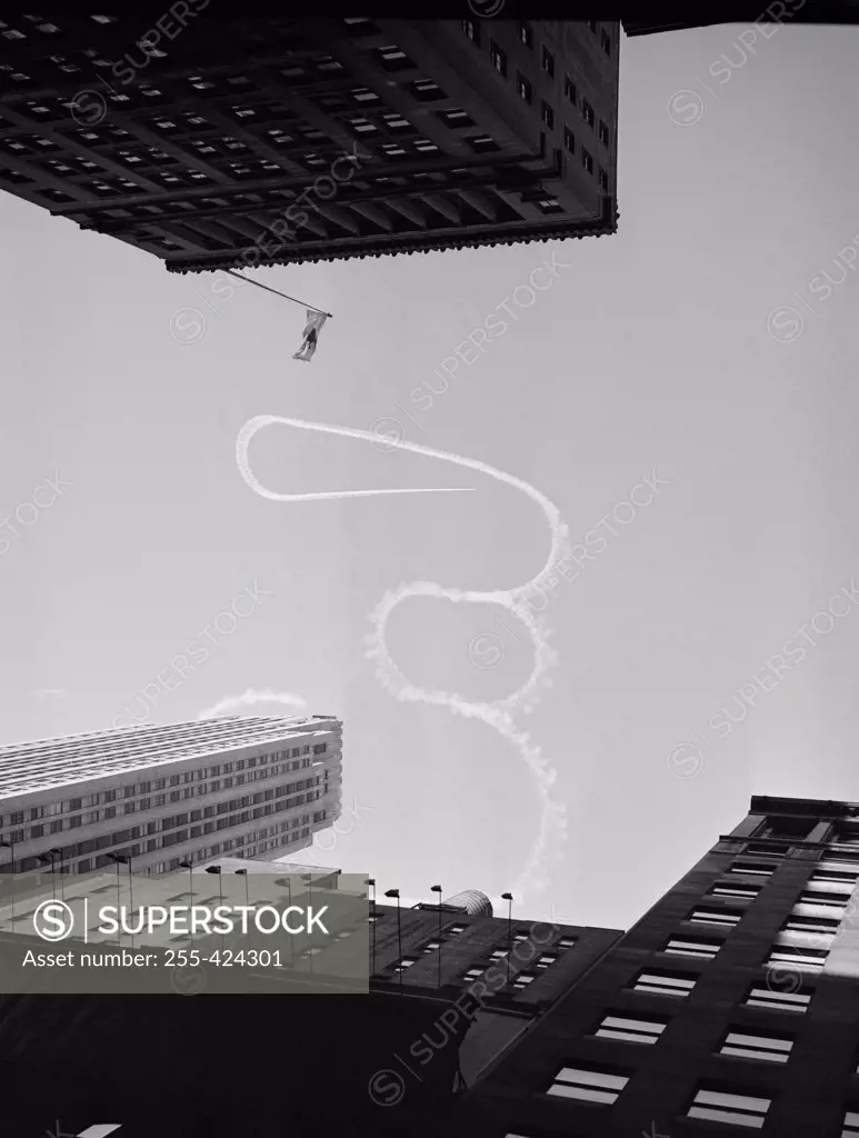 USA, New York City, Upward view of acrobatic aeroplane vapor trail over skyscrapers