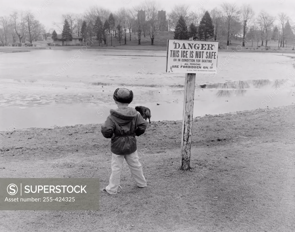 Rear view of boy standing at edge of semi-frozen lake