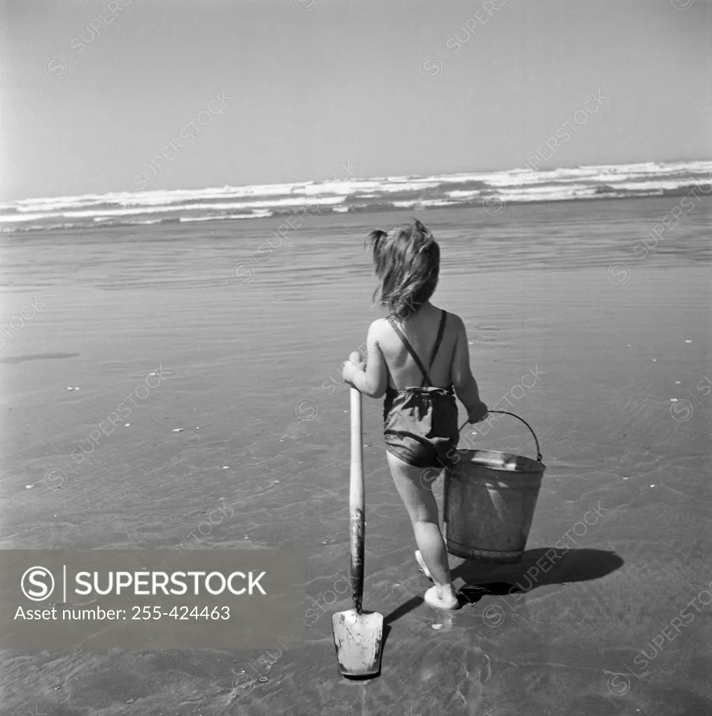 Girl holding bucket and shovel walking towards sea