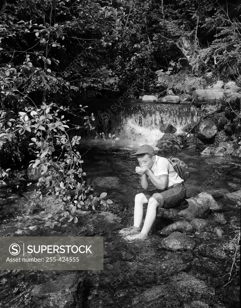 Boy sitting and drinking water from mountain stream