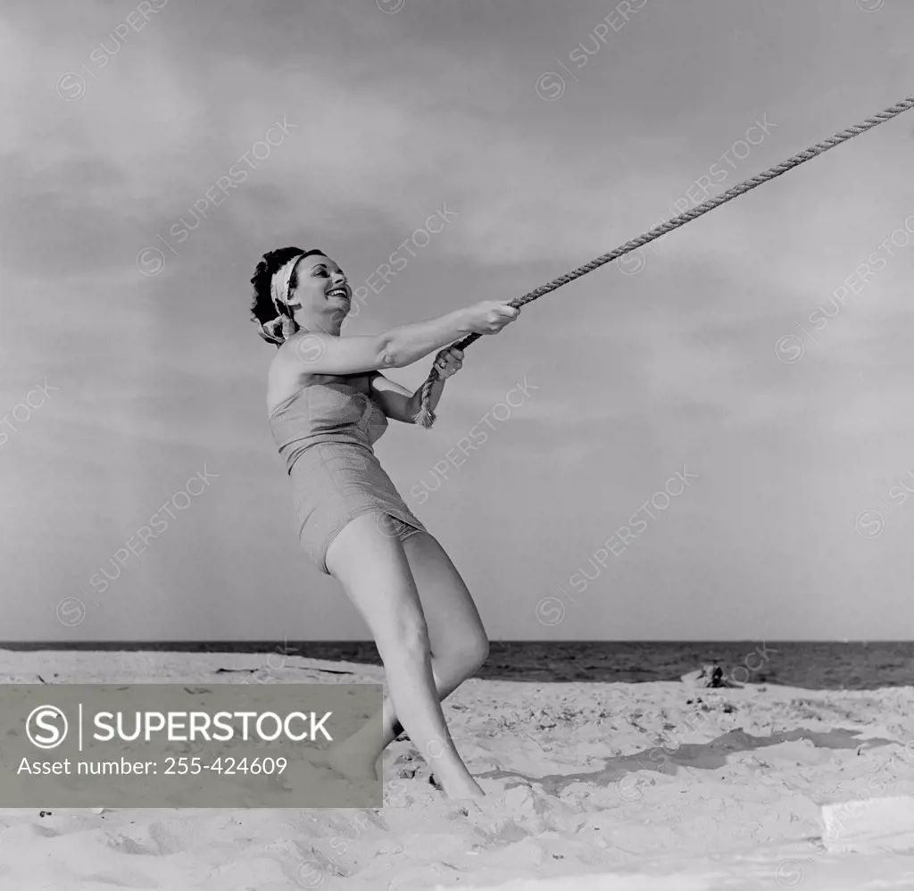 Young happy woman pulling rope at beach