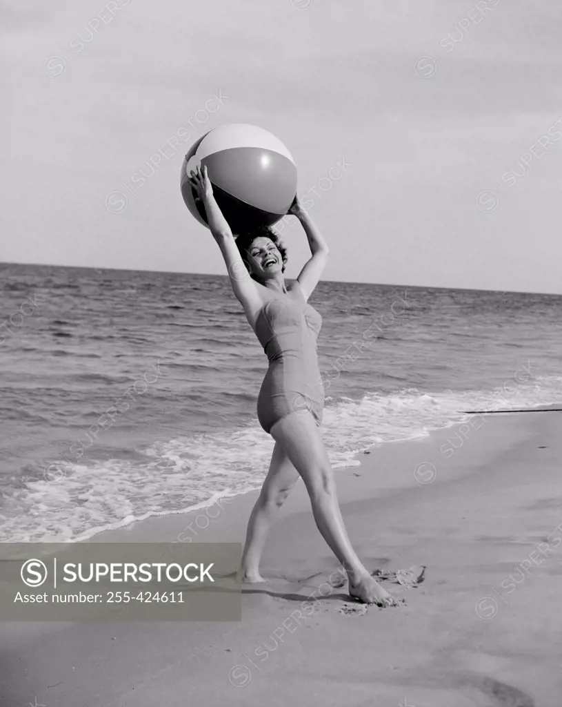 Young happy woman holding beach ball and looking at camera at beach