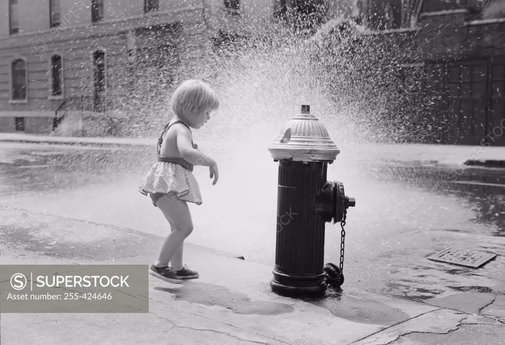 Little girl cooling off at fire hydrant on street