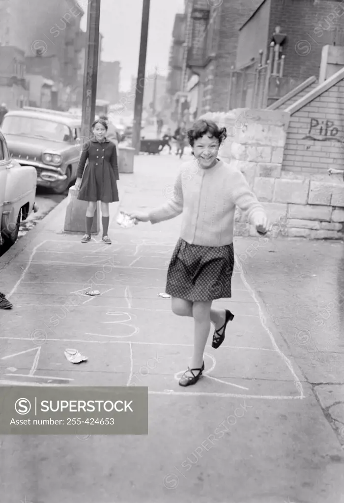 Two girls playing hop-scotch on street