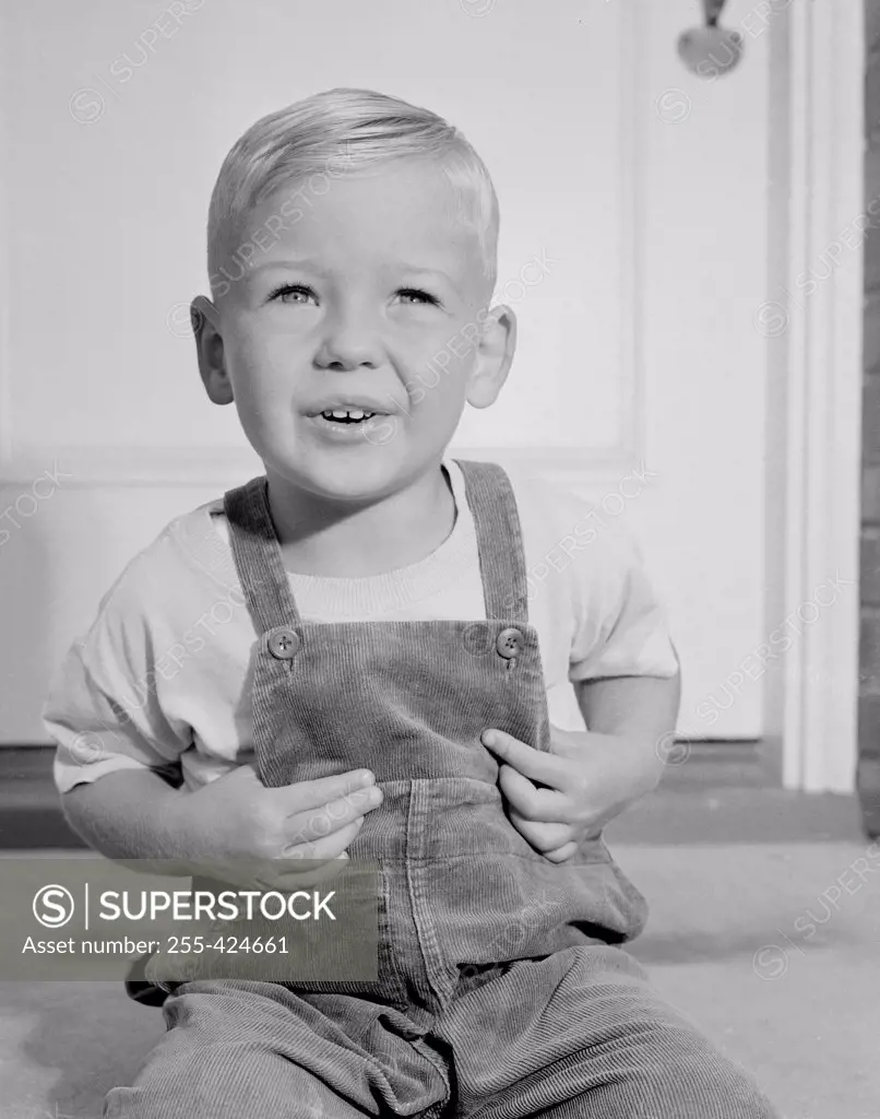 Portrait of small boy in overalls sitting in front of home entrance