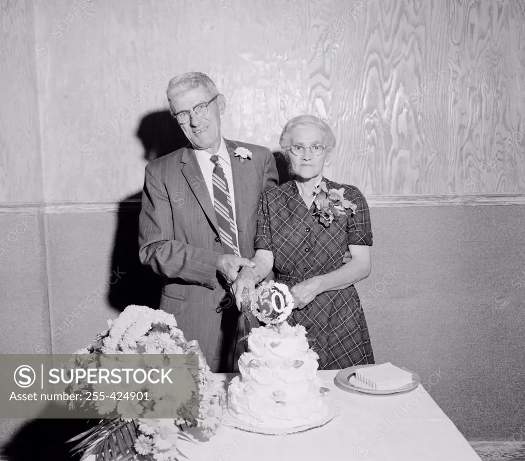 Portrait of senior couple cutting 50th wedding anniversary cake