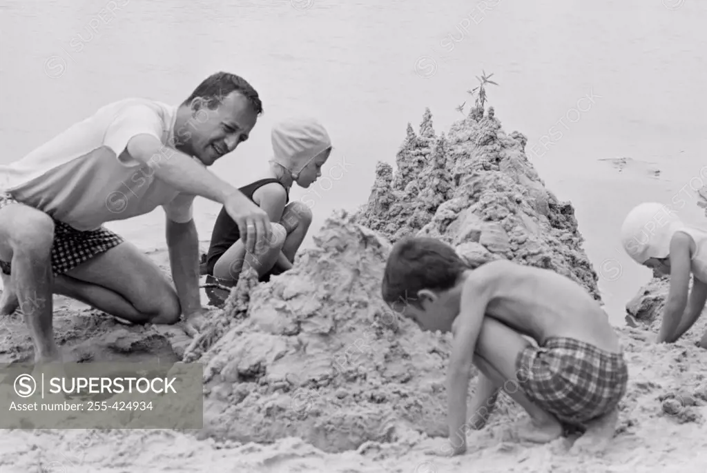 Father with three children building sand castle on beach