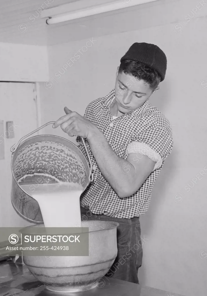 Young man straining milk into milk churn