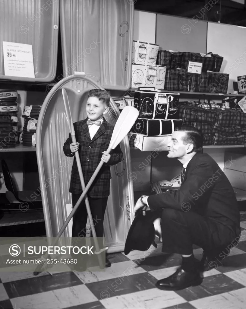 Boy holding two oars in a store and a salesman looking at him