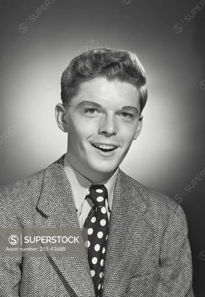 Vintage Photograph. Teenage boy in blazer and polka dot tie with mouth open in comical smile expression
