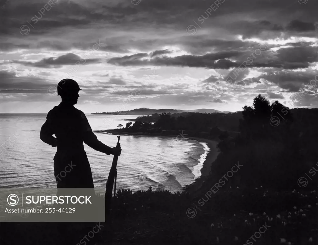Silhouette of an army soldier standing with gun at dusk