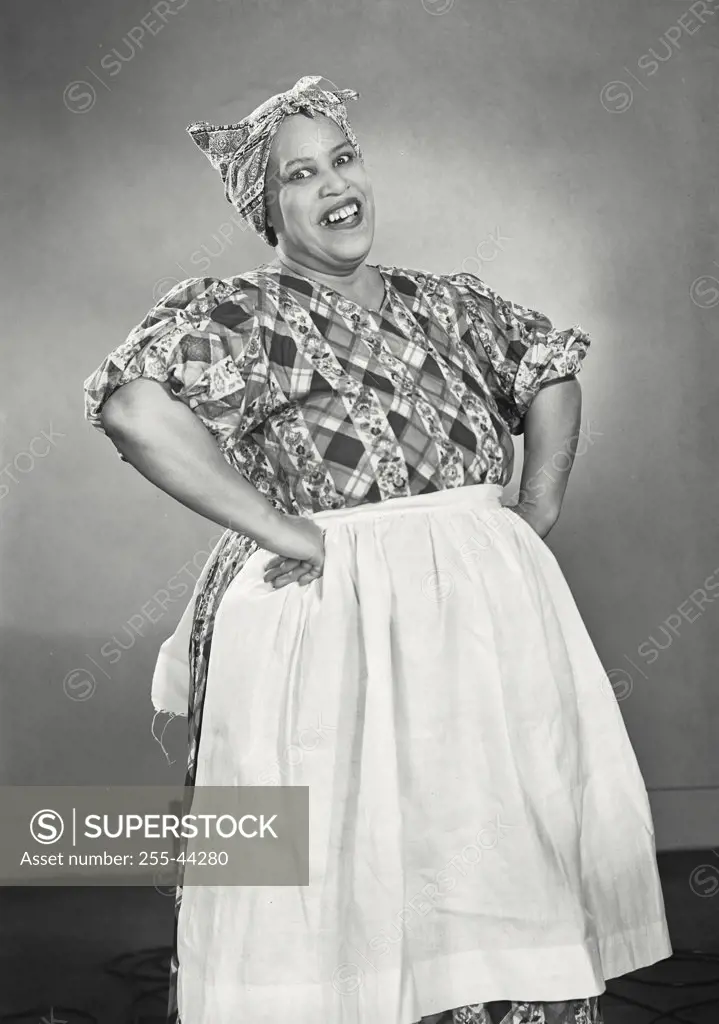 African American woman wearing head scarf and apron holding hands on hips smiling