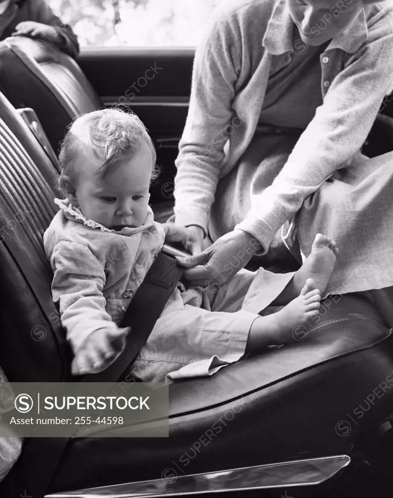 Mid adult woman fastening her daughter's car seat belt