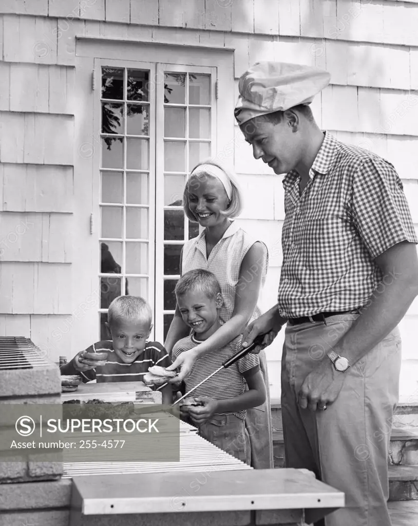 Side profile of a mid adult man cooking food with his wife and two children standing beside him