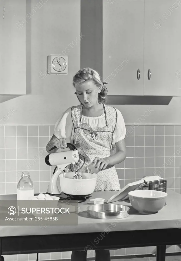 Vintage photograph. Young woman using an egg beater in a domestic kitchen