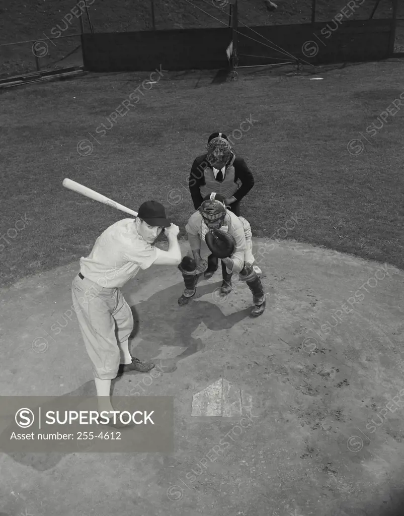 Vintage Photograph. Baseball player swinging baseball bat with baseball catcher and baseball umpire squatting beside him